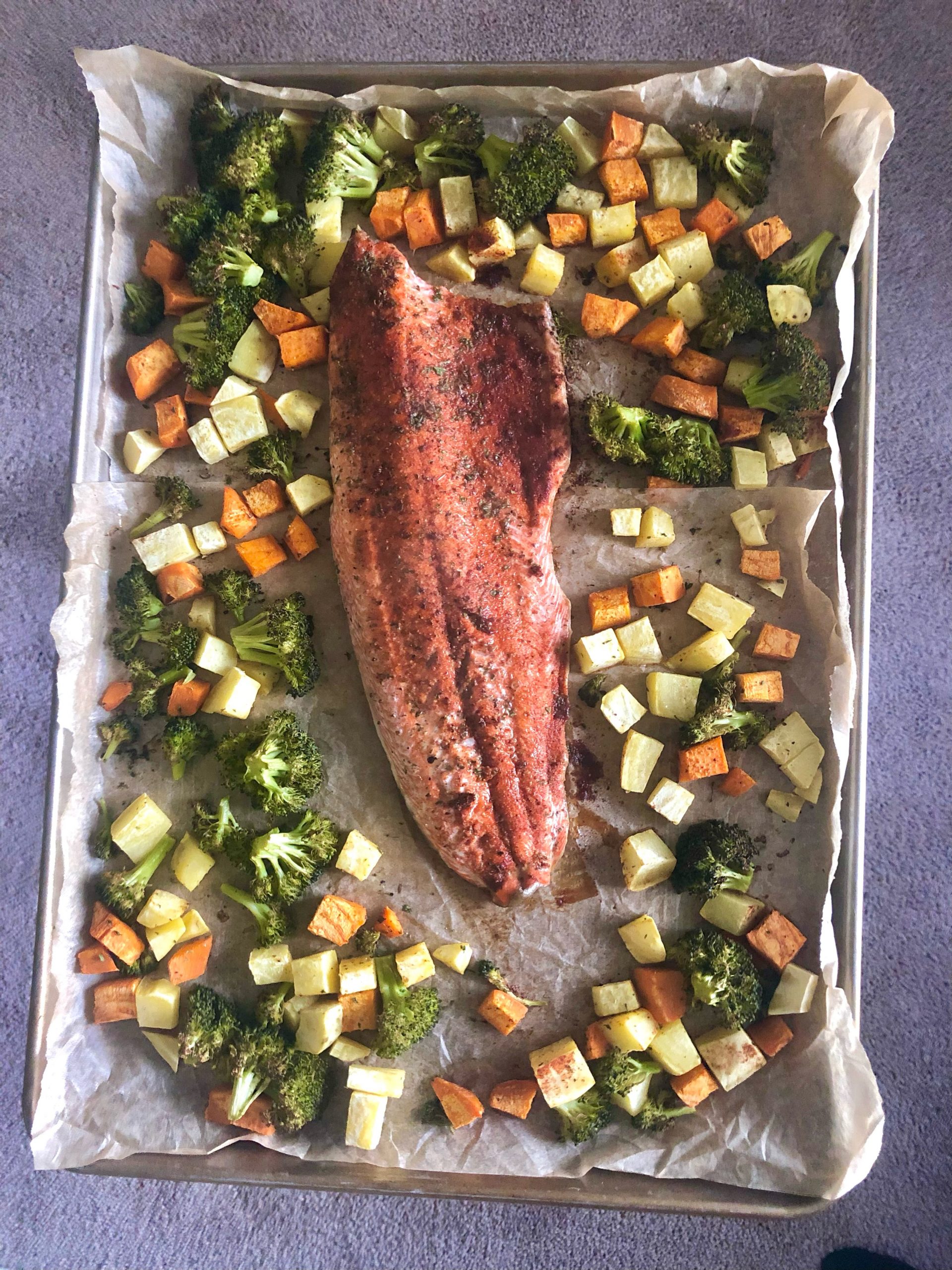 Pan with large spiced fish surrounded by broccoli, cubed potato, and cubed sweet potato
