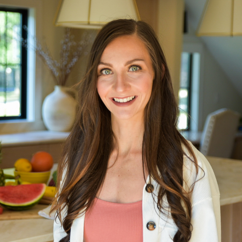 smiling woman with long dark brown hair and big green eyes, wearing a pink tank top under a white sweater with tortoise shell buttons