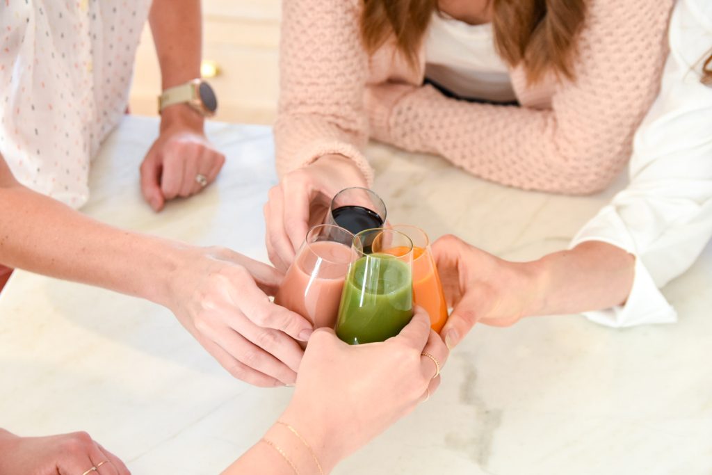 Four hands each clinking together glasses filled with different smoothies