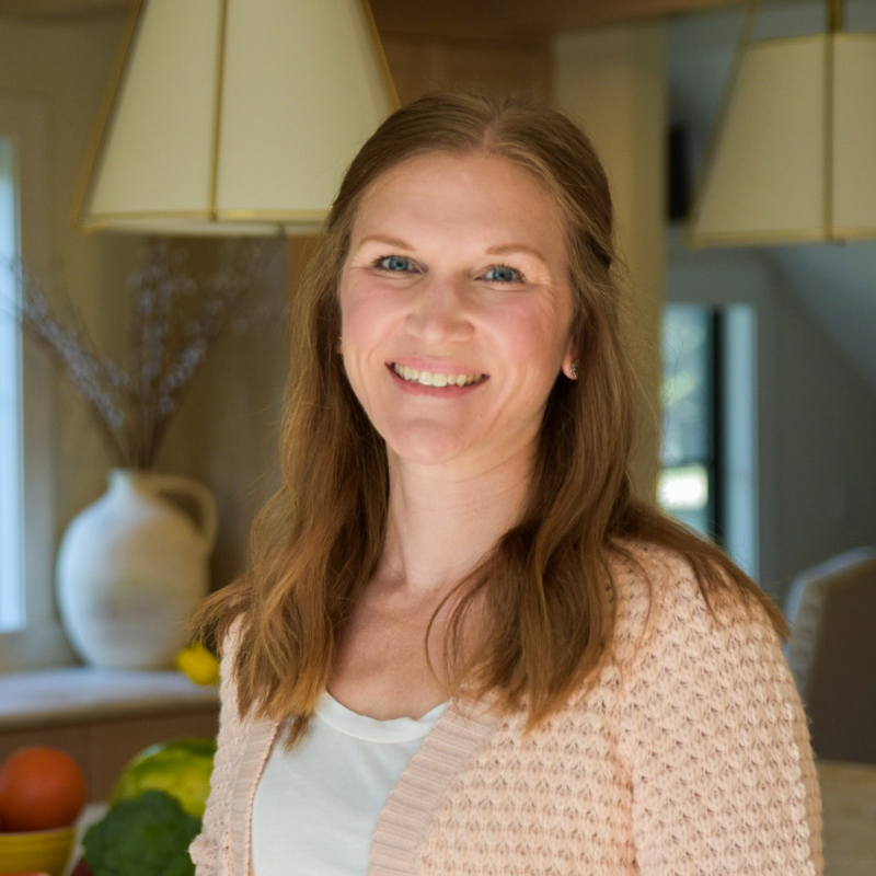 smiling woman with light brown hair pulled half back wearing a white t-shirt under a pink knit cardigan