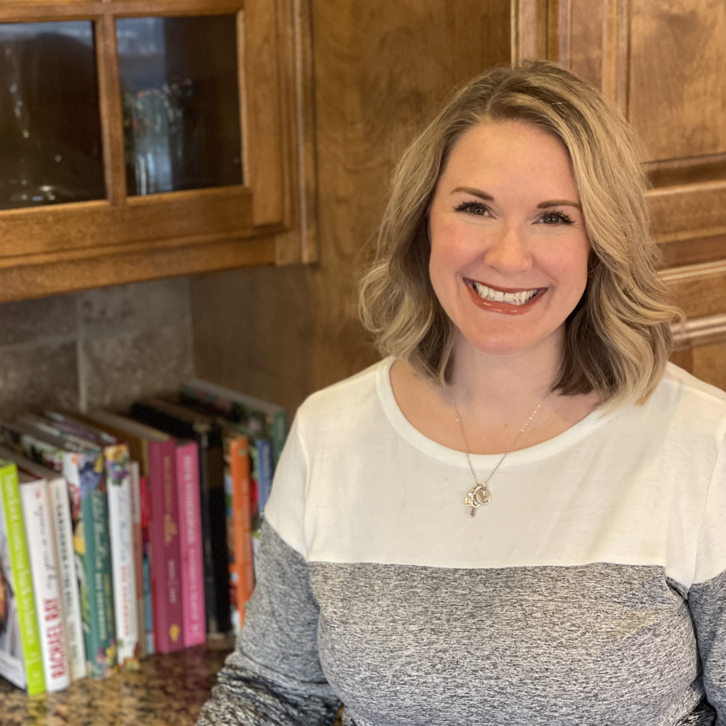 smiling white woman with shoulder length dirty blonde hair parted to one side, sweater, and necklace